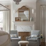 White bedroom with a four-poster bed, marble fireplace, and upholstered chairs.