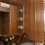Bathroom with brick wall, wooden slats, and gold sconces.