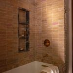 Tiled shower with pink and brown ceramic tiles, brass fixtures, and a shelf.