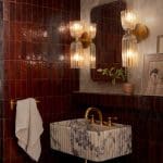 Red brick wall with gold sconces and mirror, marble sink.