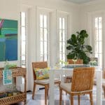 White dining area with rattan chairs, bar cart, and large ficus tree.