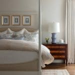 Cream-colored bed with blue and white pillows, wooden nightstand, and framed artwork.