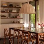 Wooden dining table with chairs, open shelving, and a large pendant light.