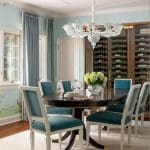 White dining table with teal chairs, chandelier, and blue wall decor.