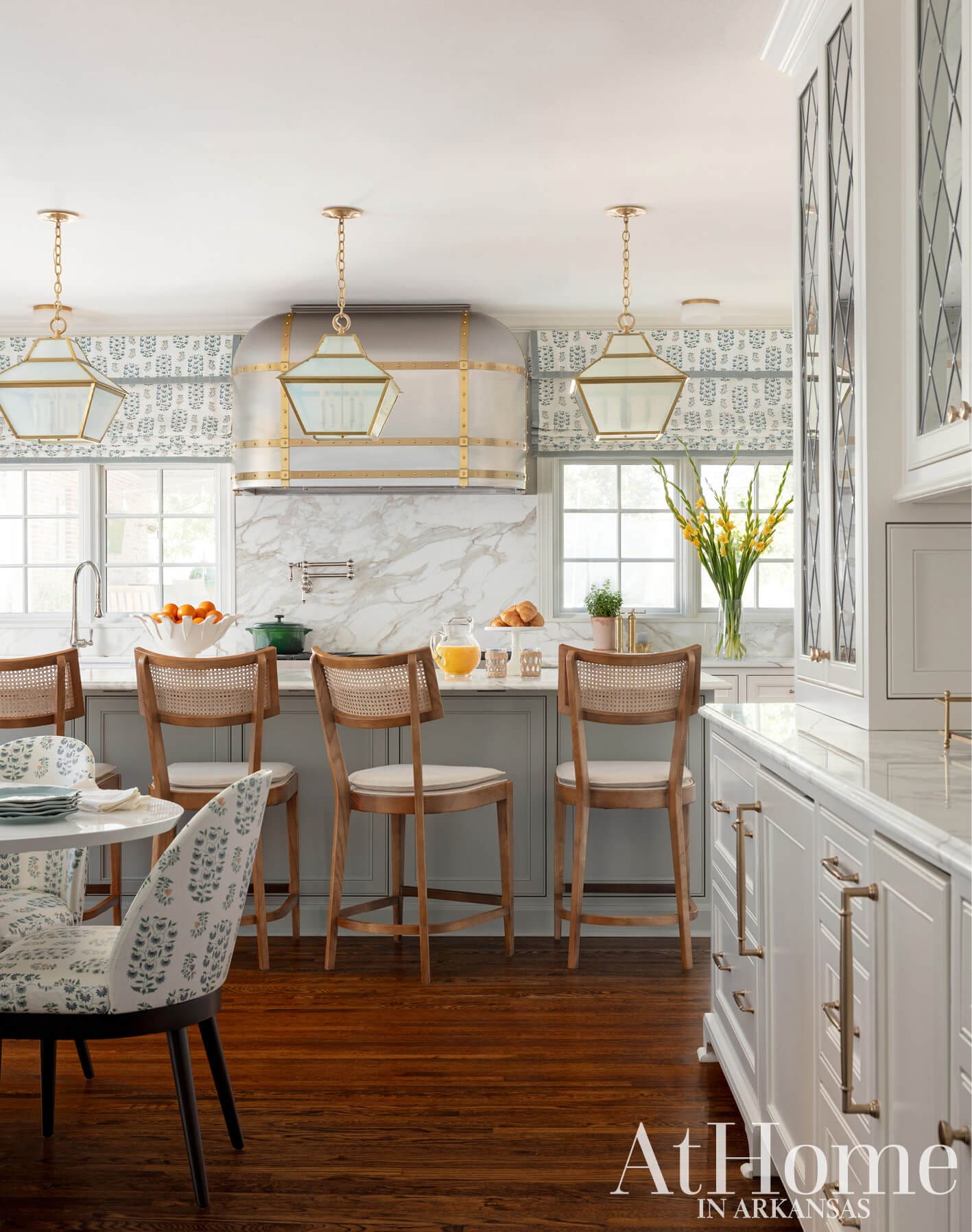 White kitchen with marble countertops, gold pendant lights, and patterned wallpaper.