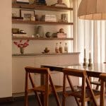 Wooden shelving unit with books and decor, dining chairs, and a table.