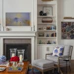 White armchair with blue and white patterned pillows, fireplace, and bookshelves.