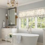 White bathroom with a chandelier, bathtub, and window.
