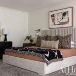 Bedroom with beige upholstered headboard, artwork, and bedding.