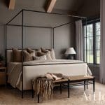 Four-poster bed with beige linens and dark metal frame.