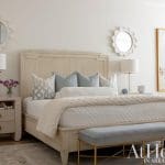 White bed with light gray bedding, mirror, and artwork.
