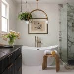 Marble bathroom with freestanding tub, gold pendant lights, and artwork.
