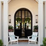 White arched entryway with black doors and outdoor seating.