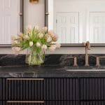 Black and white tile backsplash with a gold faucet and tulips.
