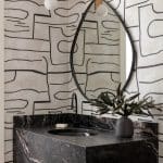Marble vanity with black and white geometric wallpaper and a circular mirror.