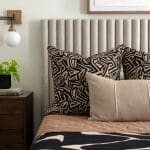 Gray upholstered headboard with patterned pillows and a wall-mounted light.