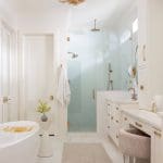 White bathroom with glass shower, gold fixtures, and a marble vanity.