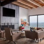 Living room with a concrete fireplace, television, and large windows overlooking water.