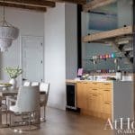Wooden bar with mirrored backsplash and glassware, chandelier, and artwork.