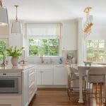 White kitchen with brass pendant lights and a wooden island.