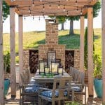 Wooden pergola with string lights over a stone outdoor dining table.