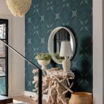 Teal patterned wallpaper, circular mirror, and driftwood console table.