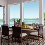 Round table with chairs, drinks, and pillows overlooking a lake.