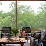Wooden deck with seating, glass windows, and greenery.