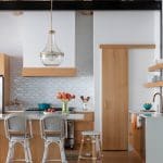 White kitchen with wood cabinetry, tile backsplash, and pendant lighting.