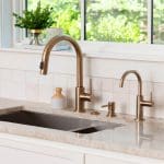 Brass faucet and sink with white tile backsplash.
