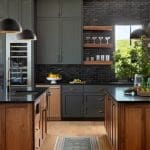 Dark green kitchen with wood cabinetry, brick backsplash, and black pendant lights.