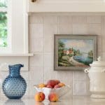 White subway tile backsplash with a framed painting and fruit.
