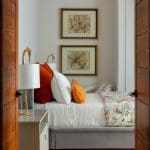 Bedroom with wooden panel walls, floral artwork, and orange pillows.