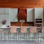 Light green kitchen cabinets with a copper range hood and leather bar stools.