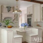 White kitchen island with seating, stone countertop, and brass fixtures.