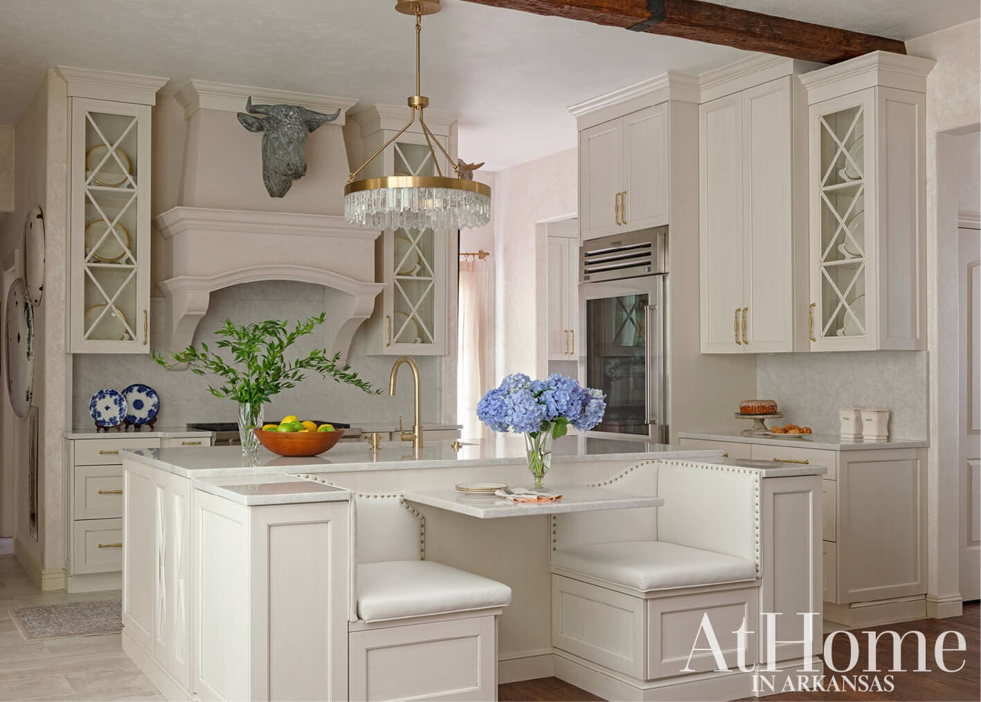 White kitchen island with seating, stone countertop, and brass fixtures.