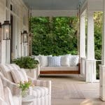 White porch with swing, lanterns, and greenery.