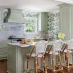 Green kitchen with marble island, rattan chairs, and wallpaper.