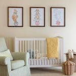 White framed artwork and a white crib in a nursery.