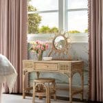 Pink woven vanity table with mirror and floral arrangement.