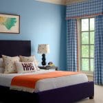Blue bedroom with a purple headboard, plaid curtains, and orange accents.