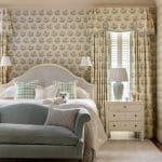 Floral wallpaper, light blue curtains, and a bed with pillows.