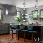 Kitchen with gray cabinetry, stainless steel range hood, and teal bar stools at a dark fluted