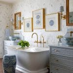 Freestanding tub in a bathroom with floral wallpaper, blue vanity, and brass fixtures.