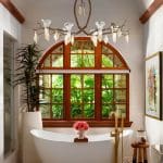 Freestanding bathtub with brass faucet under arched window, surrounded by river stones.