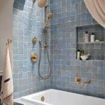Blue tiled shower with brass fixtures and white bathtub