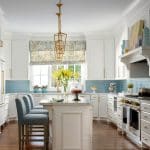 White kitchen with blue subway tile backsplash, marble island, and gold pendant light.