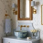 Powder room with floral wallpaper, blue and white bowl sink, brass fixtures, and checkered sconce