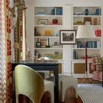 Green upholstered chair at desk with puzzle, flanked by patterned curtains and built-in bookshelves.
