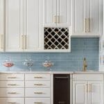 White kitchen with blue subway tile backsplash, wine rack, and gold hardware.
